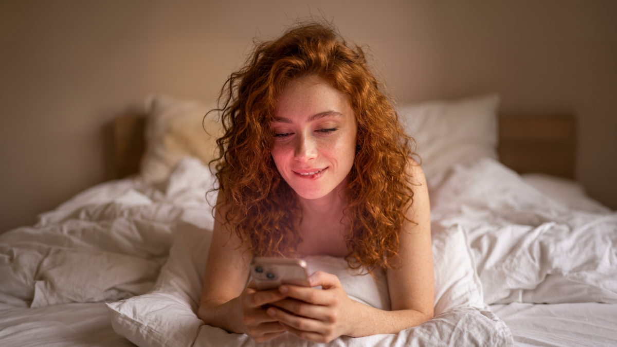 A woman smiling softly at her phone in warm light